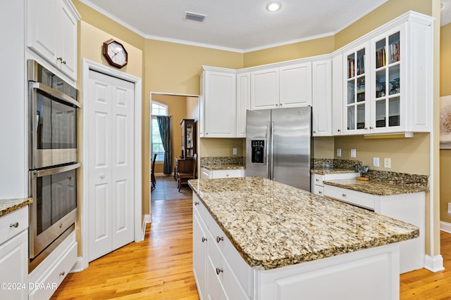 kitchen featuring crown molding, appliances with stainless steel finishes, light stone countertops, white cabinets, and light hardwood / wood-style flooring