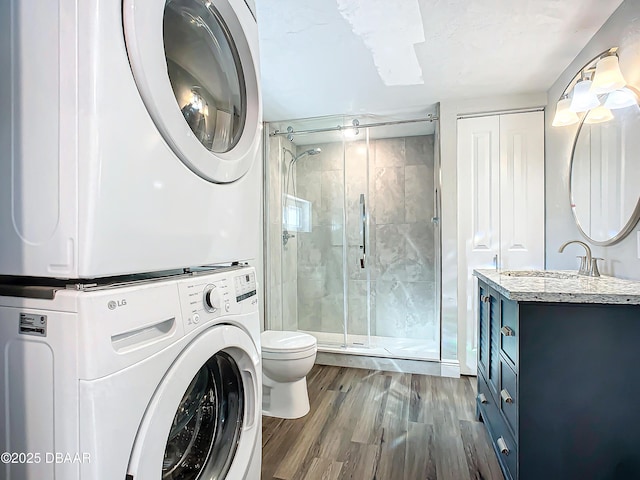 bathroom featuring vanity, toilet, walk in shower, stacked washer / drying machine, and wood-type flooring