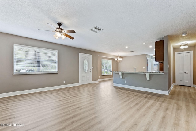 unfurnished living room featuring ceiling fan with notable chandelier, a textured ceiling, and light wood-type flooring