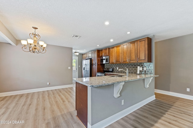 kitchen featuring stainless steel appliances, light wood-type flooring, hanging light fixtures, sink, and kitchen peninsula