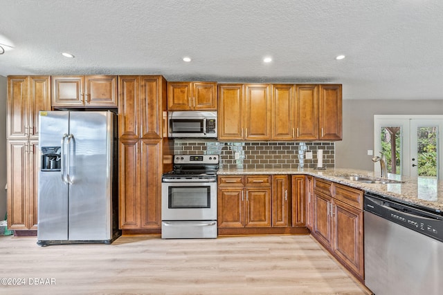 kitchen with stainless steel appliances, a textured ceiling, light stone countertops, sink, and light hardwood / wood-style flooring