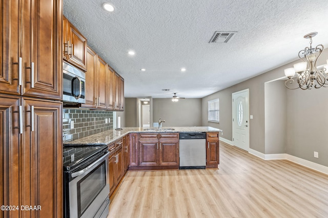 kitchen featuring stainless steel appliances, sink, kitchen peninsula, a textured ceiling, and light hardwood / wood-style flooring