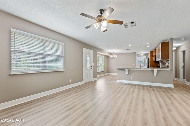 unfurnished living room featuring ceiling fan with notable chandelier, a textured ceiling, and light wood-type flooring