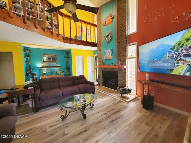 living room featuring a fireplace, a towering ceiling, wood-type flooring, and ceiling fan