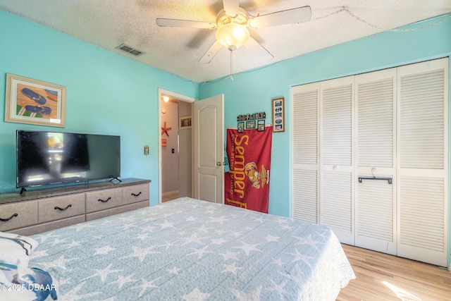 bedroom featuring visible vents, light wood-style flooring, a textured ceiling, a closet, and ceiling fan