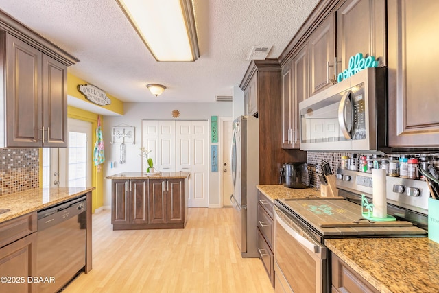 kitchen with visible vents, backsplash, light stone counters, appliances with stainless steel finishes, and light wood-style floors