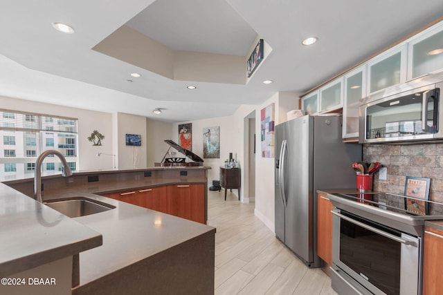 kitchen with sink, appliances with stainless steel finishes, backsplash, a raised ceiling, and light hardwood / wood-style flooring