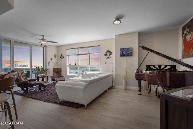 living room with ceiling fan, a textured ceiling, and light wood-type flooring