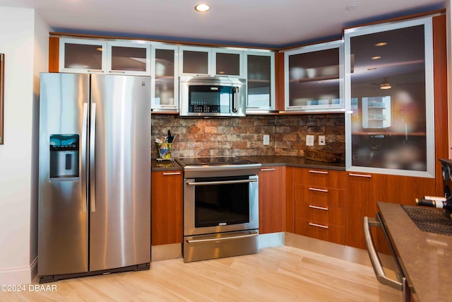 241 Riverside Dr Unit 1401-2, Holly Hill, FL 32117 - kitchen featuring stainless steel appliances, tasteful backsplash, brown cabinets, glass insert cabinets, and dark countertops