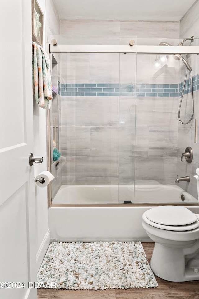 bathroom featuring toilet, hardwood / wood-style flooring, and shower / bath combination with glass door