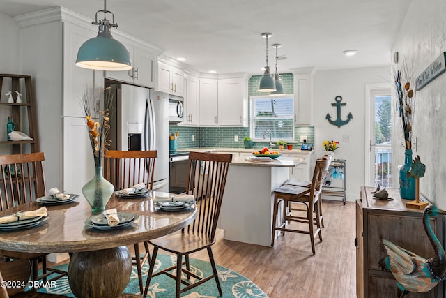 kitchen featuring white cabinetry, appliances with stainless steel finishes, hanging light fixtures, a breakfast bar area, and light hardwood / wood-style flooring