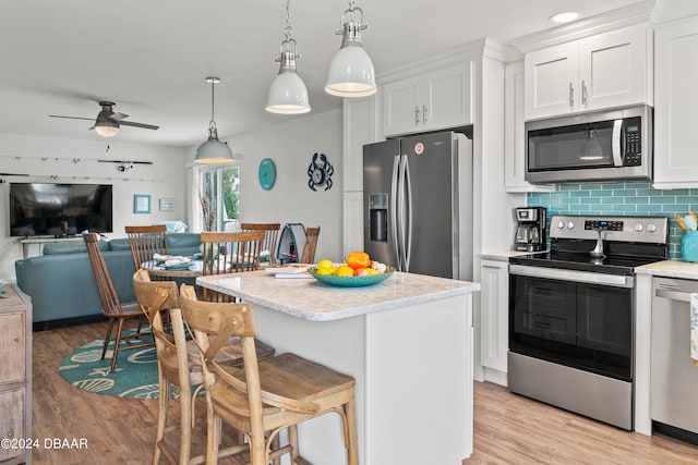 kitchen with stainless steel appliances, white cabinetry, decorative light fixtures, ceiling fan, and light hardwood / wood-style flooring