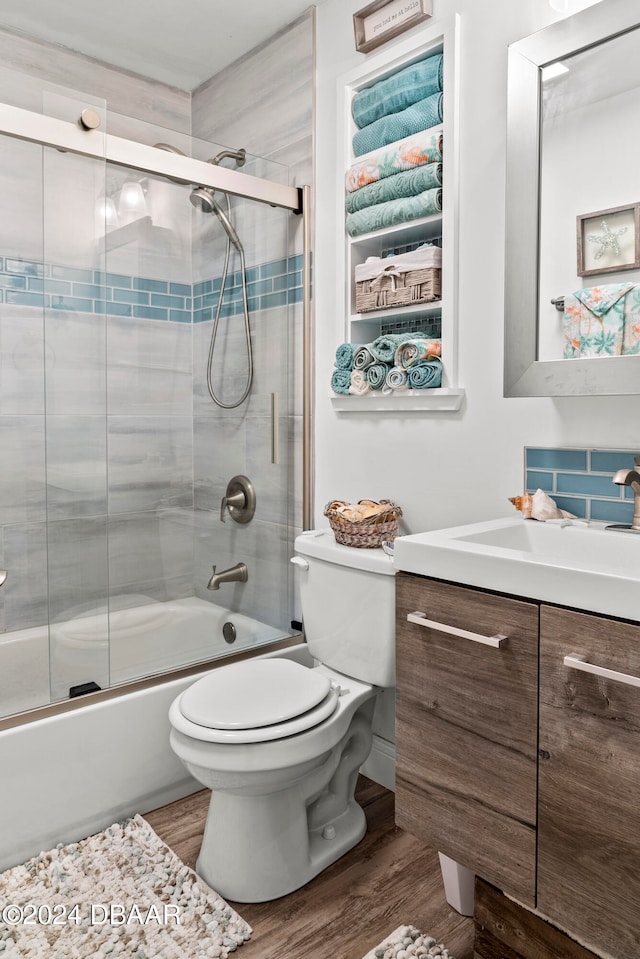 full bathroom featuring hardwood / wood-style flooring, bath / shower combo with glass door, vanity, and toilet