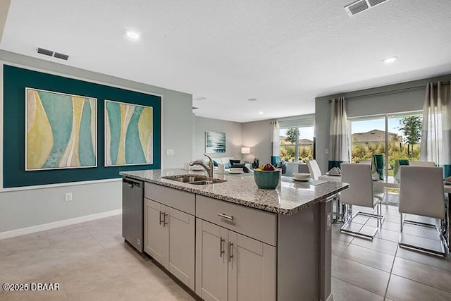 kitchen featuring light stone countertops, dishwasher, an island with sink, sink, and gray cabinets