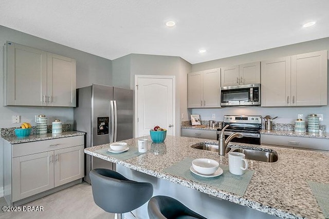 kitchen with sink, a breakfast bar, stainless steel appliances, light stone counters, and gray cabinets