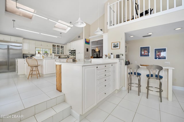 kitchen with a breakfast bar, high vaulted ceiling, white cabinets, appliances with stainless steel finishes, and decorative light fixtures