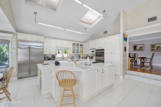 kitchen featuring a kitchen breakfast bar, stainless steel appliances, a kitchen island with sink, light tile patterned floors, and white cabinetry