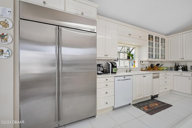 kitchen featuring sink, light tile patterned floors, built in refrigerator, white dishwasher, and white cabinets