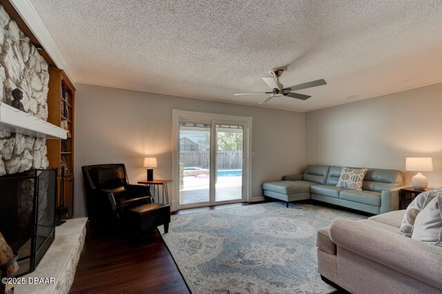 living room with ceiling fan, a stone fireplace, a textured ceiling, and wood finished floors