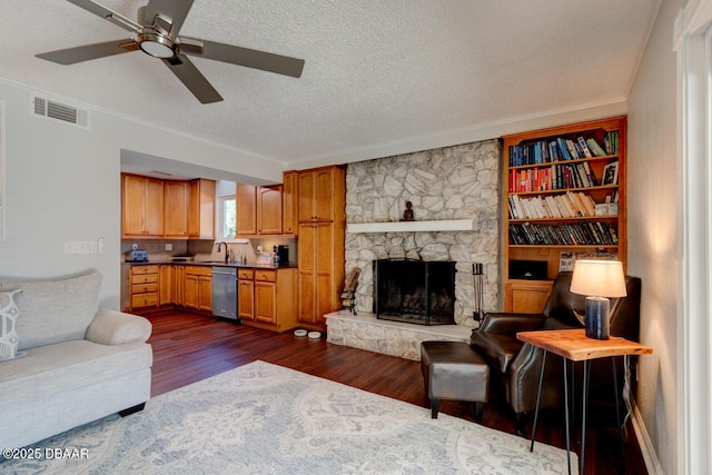 living area with crown molding, dark wood finished floors, visible vents, a stone fireplace, and a textured ceiling