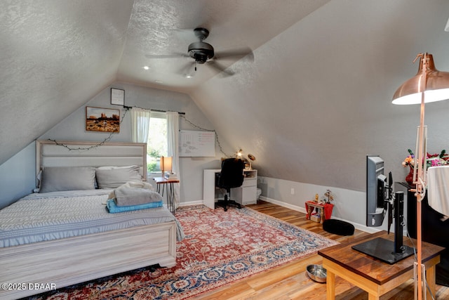 bedroom with a ceiling fan, vaulted ceiling, a textured ceiling, wood finished floors, and baseboards