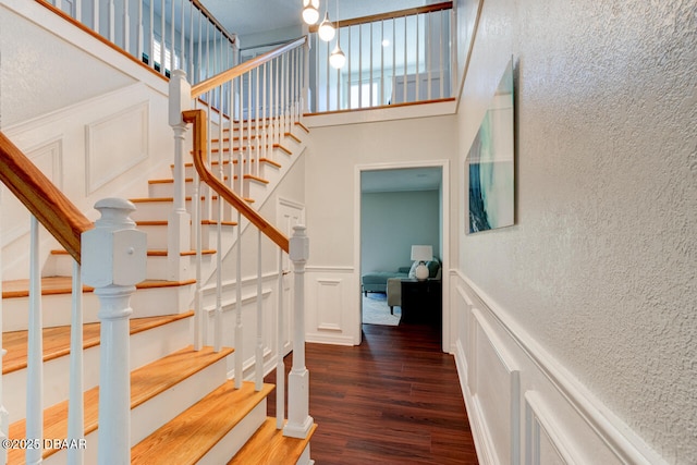 stairway featuring a towering ceiling, a decorative wall, wood finished floors, and a textured wall