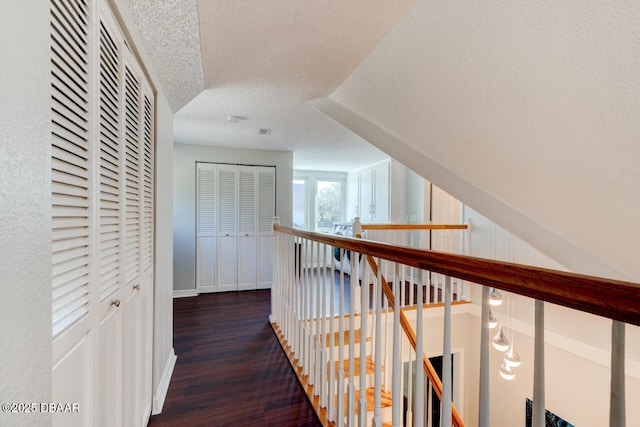 hall featuring visible vents, a textured ceiling, an upstairs landing, and wood finished floors