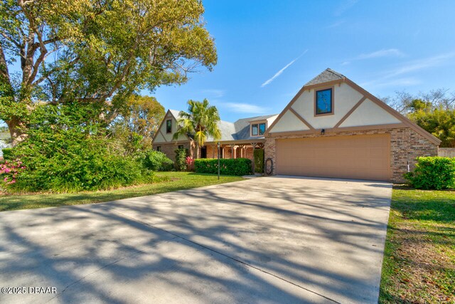 tudor-style house with a garage, concrete driveway, brick siding, and stucco siding