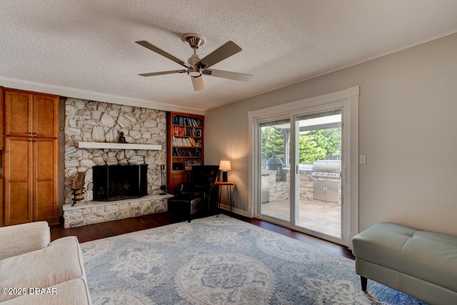 living room featuring a textured ceiling, ceiling fan, a stone fireplace, wood finished floors, and crown molding