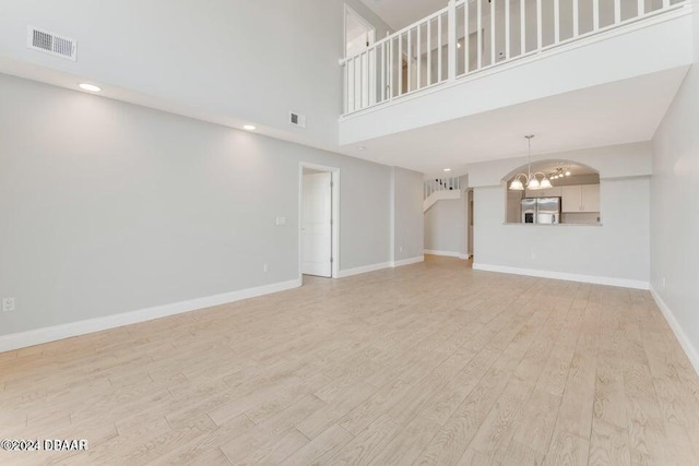 unfurnished living room featuring a notable chandelier, light hardwood / wood-style floors, and a high ceiling