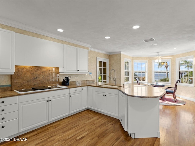 kitchen with kitchen peninsula, light wood-type flooring, sink, stovetop, and white cabinets