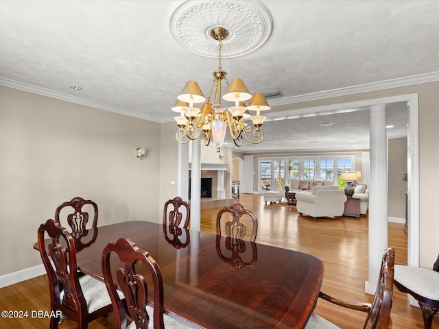 dining area with decorative columns, ornamental molding, an inviting chandelier, hardwood / wood-style floors, and a tiled fireplace