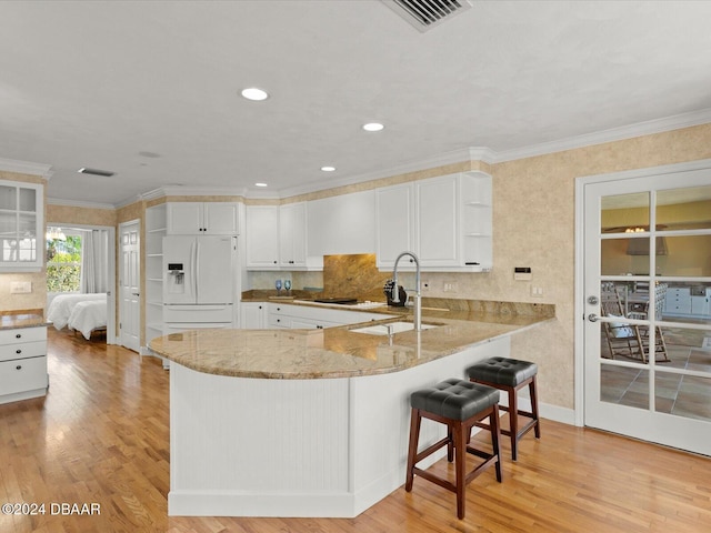 kitchen with sink, white refrigerator with ice dispenser, kitchen peninsula, white cabinets, and light wood-type flooring