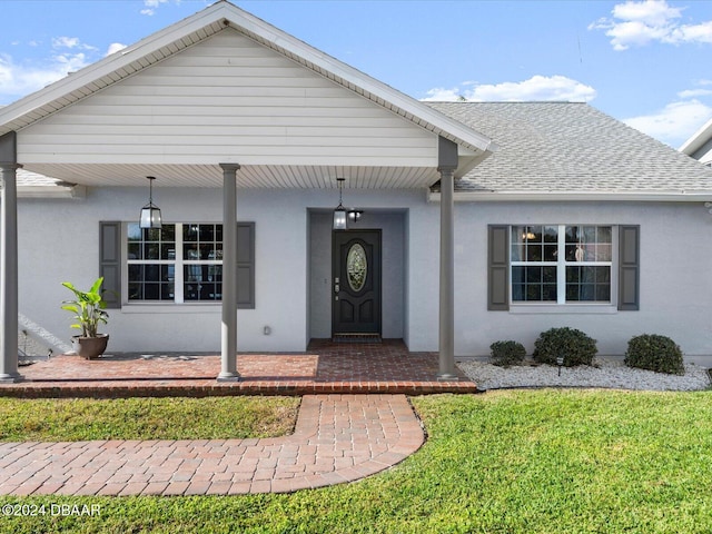 entrance to property with covered porch and a lawn