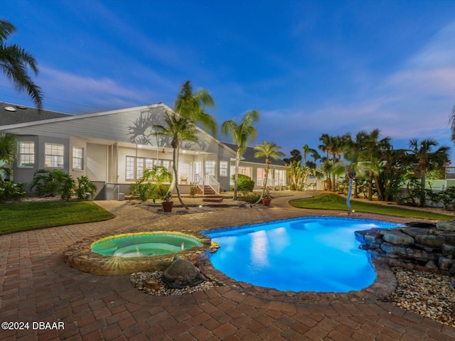 pool at dusk featuring an in ground hot tub, french doors, and a patio