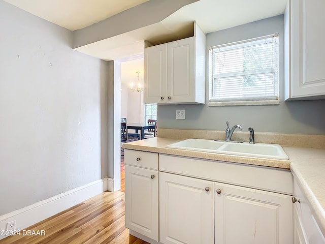 kitchen with white cabinetry, light wood-type flooring, sink, and an inviting chandelier