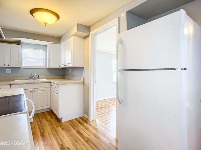 kitchen with white cabinets, light hardwood / wood-style floors, and white fridge