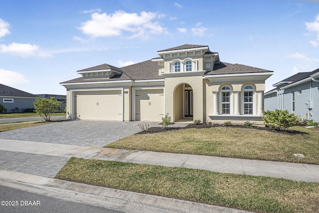 mediterranean / spanish-style house with stucco siding, decorative driveway, a front yard, a shingled roof, and a garage