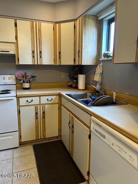 kitchen with under cabinet range hood, light countertops, light tile patterned floors, white appliances, and a sink