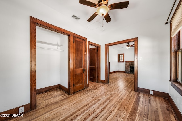 unfurnished bedroom featuring light wood-type flooring, a closet, a brick fireplace, and ceiling fan