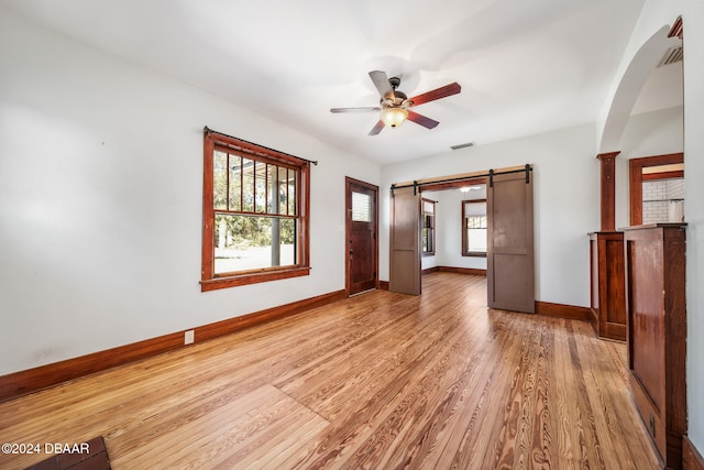 empty room with ceiling fan, a barn door, light hardwood / wood-style floors, and a wealth of natural light