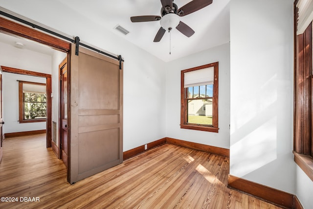 unfurnished bedroom featuring a barn door, light hardwood / wood-style flooring, and ceiling fan