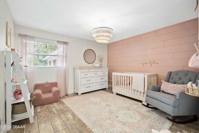 bedroom with wooden walls, a nursery area, an inviting chandelier, and light hardwood / wood-style flooring