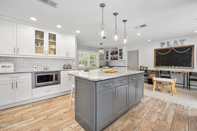 kitchen with light hardwood / wood-style floors, stainless steel microwave, white cabinets, gray cabinets, and pendant lighting