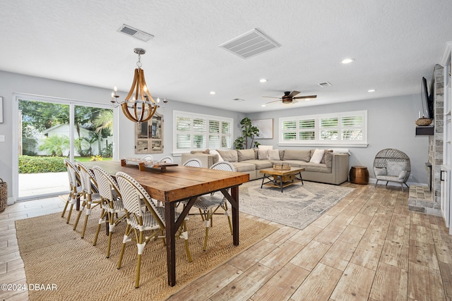 dining space with ceiling fan with notable chandelier, a textured ceiling, and light wood-type flooring