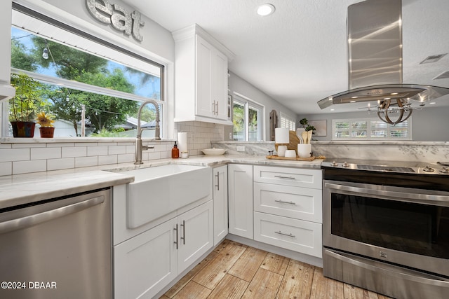 kitchen with island range hood, white cabinetry, appliances with stainless steel finishes, backsplash, and light stone countertops