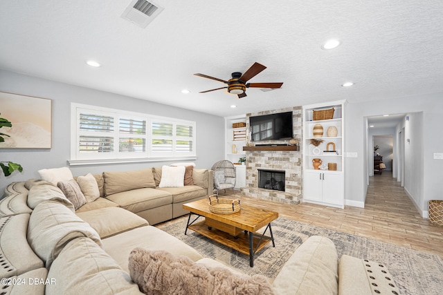 living room featuring a fireplace, light hardwood / wood-style floors, ceiling fan, and a textured ceiling