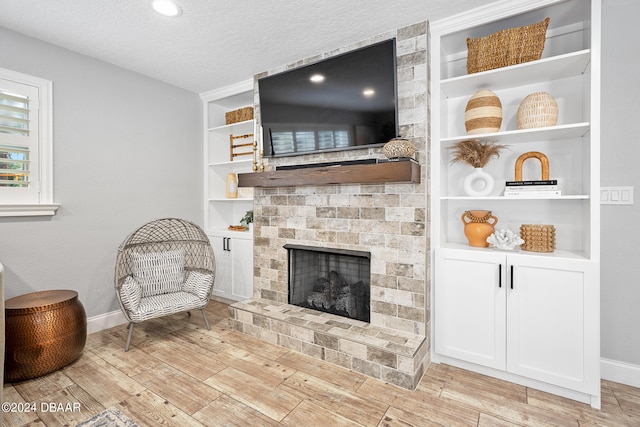 living room with a fireplace, built in features, a textured ceiling, and light wood-type flooring