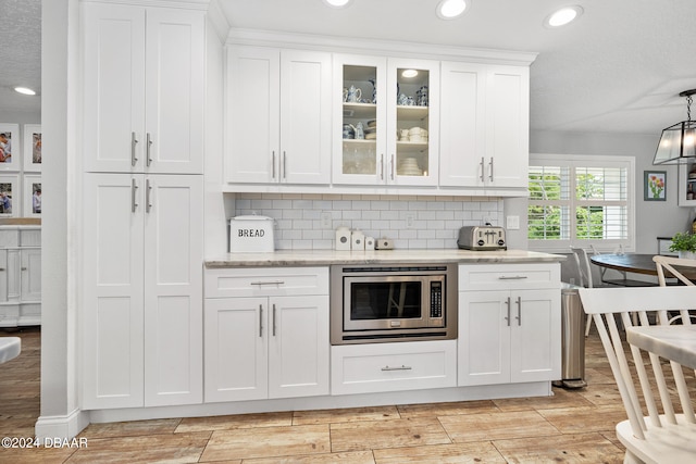 kitchen with light wood-type flooring, stainless steel microwave, decorative backsplash, and white cabinets