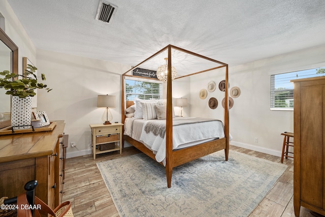 bedroom with multiple windows, a textured ceiling, and light hardwood / wood-style flooring